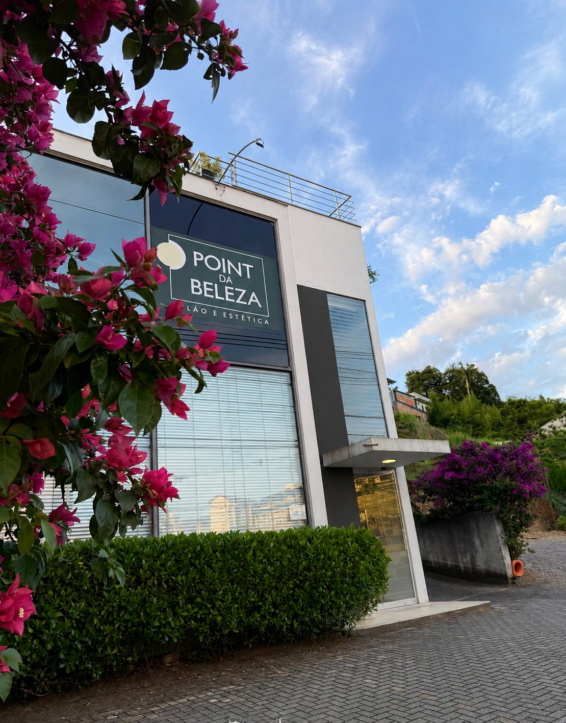 Fachada do Point da Beleza em Blumenau, com flores e céu azul.